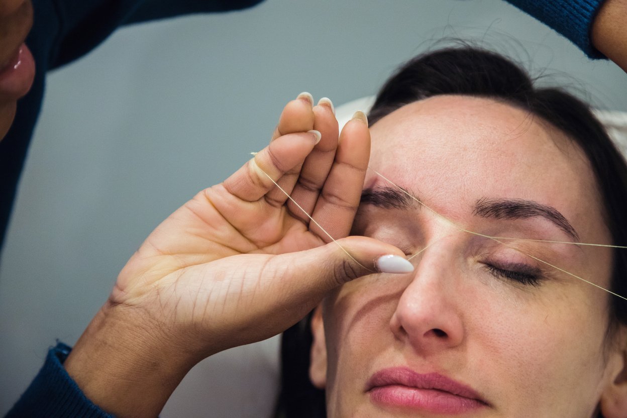 Caucasian woman removing hair from eyebrows with thread technique done by eyebrow stylist. Threading. Process Steps. Close up